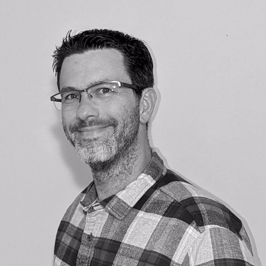 Black-and-white photograph of a person with dark short hair, glasses, and short facial hair wearing a flannel shirt.