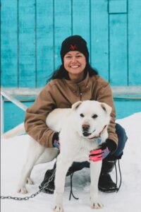 Photo of Dr. Tuma kneeling outdoors beside a white dog